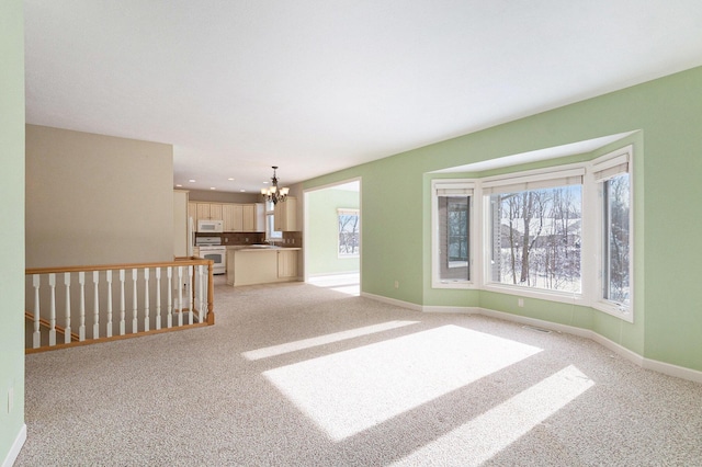 unfurnished living room featuring light carpet, a notable chandelier, baseboards, and a sink