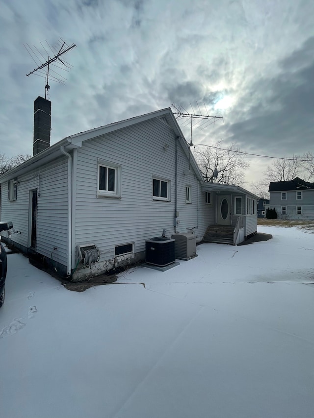 view of snowy exterior featuring central AC and a chimney