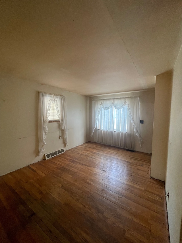 empty room with plenty of natural light, visible vents, and wood finished floors