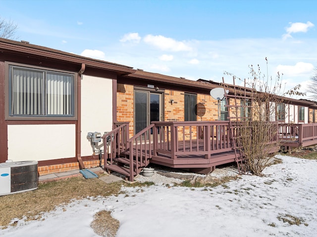 snow covered back of property with central air condition unit and a deck