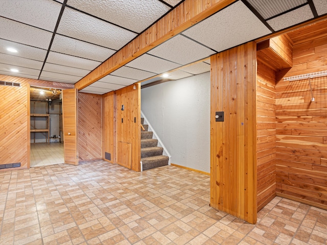 basement featuring a drop ceiling and wood walls