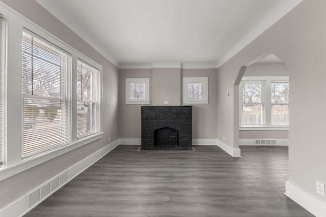 unfurnished living room featuring dark wood-type flooring, a healthy amount of sunlight, and a brick fireplace