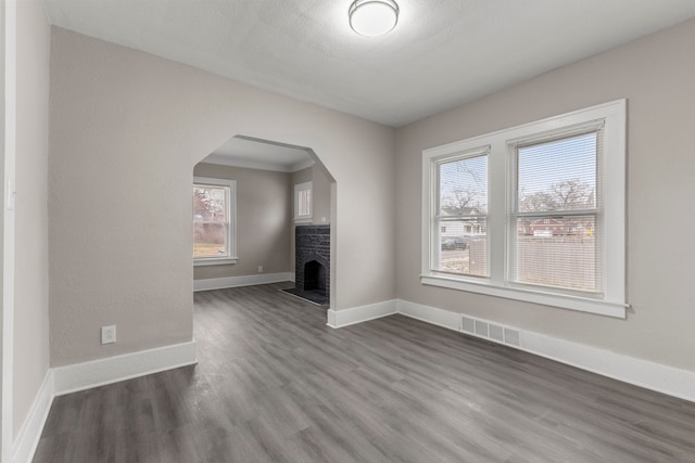 unfurnished living room featuring a brick fireplace, a textured ceiling, and dark hardwood / wood-style flooring