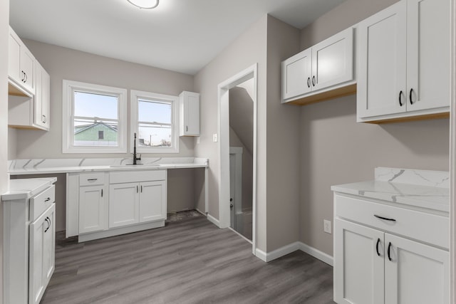 kitchen with wood-type flooring, sink, white cabinets, and light stone counters