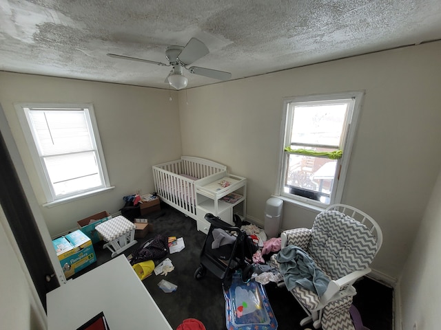 bedroom featuring ceiling fan, carpet floors, a textured ceiling, and a crib