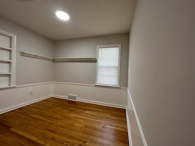 empty room featuring built in features, visible vents, baseboards, and wood finished floors