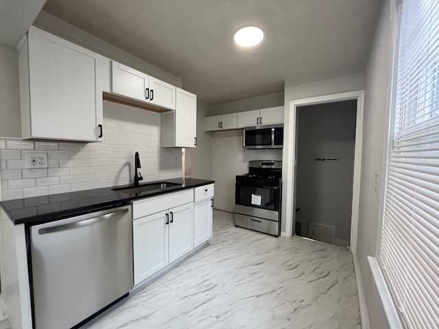 kitchen with white cabinets, dark countertops, appliances with stainless steel finishes, marble finish floor, and a sink