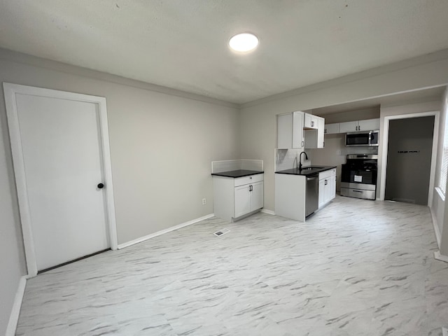 kitchen with a sink, white cabinetry, marble finish floor, appliances with stainless steel finishes, and dark countertops