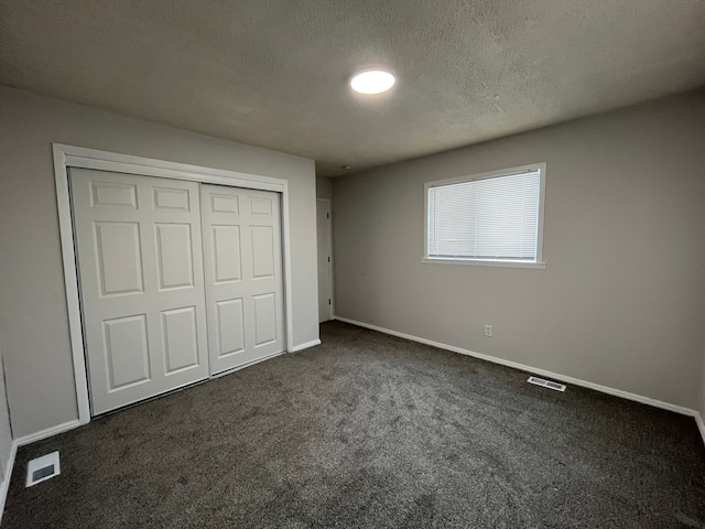 unfurnished bedroom with a textured ceiling, dark colored carpet, a closet, and visible vents