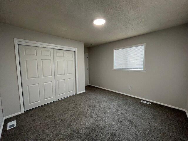 unfurnished bedroom featuring a textured ceiling, a closet, and dark colored carpet