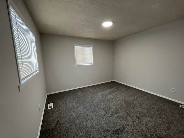 unfurnished room featuring baseboards, dark colored carpet, visible vents, and a healthy amount of sunlight