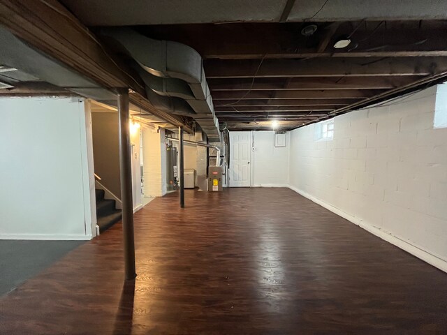 below grade area featuring heating unit, gas water heater, stairway, and dark wood-style flooring