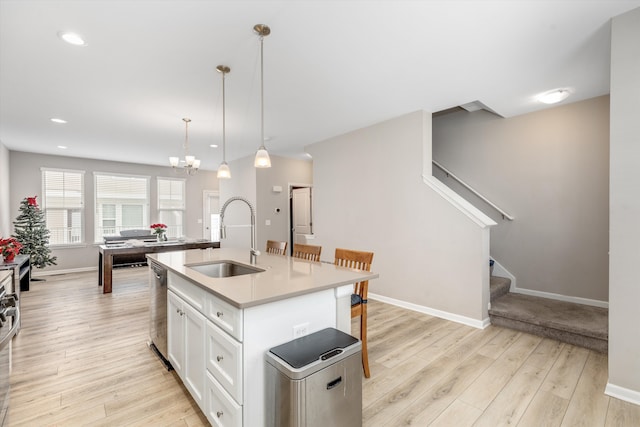 kitchen featuring sink, dishwasher, hanging light fixtures, white cabinets, and a center island with sink