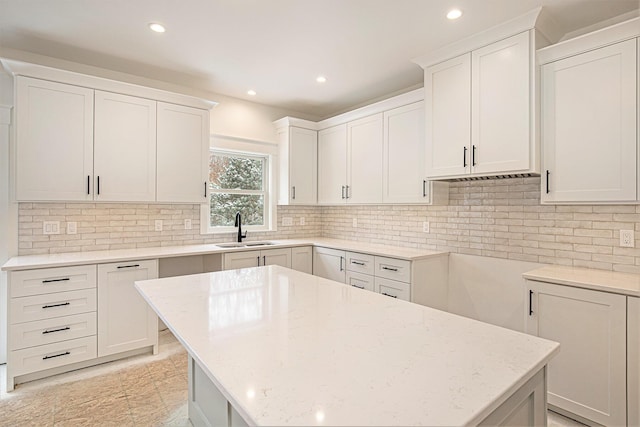 kitchen featuring sink, light stone counters, white cabinets, and backsplash