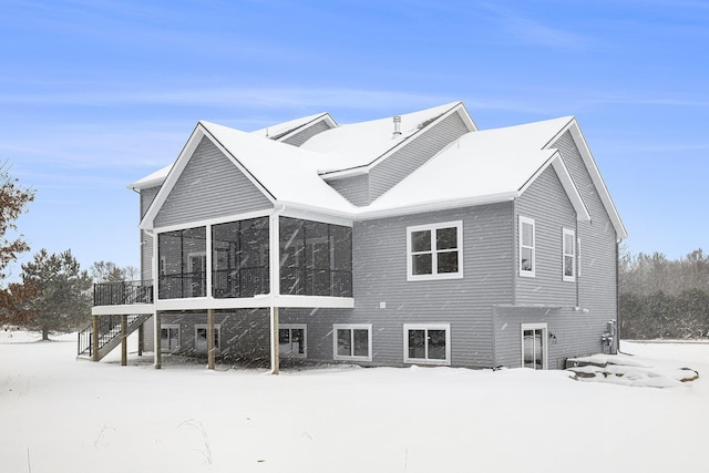 snow covered back of property featuring a sunroom