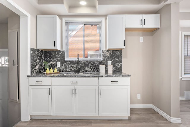 kitchen with sink, backsplash, white cabinets, dark stone counters, and light hardwood / wood-style floors