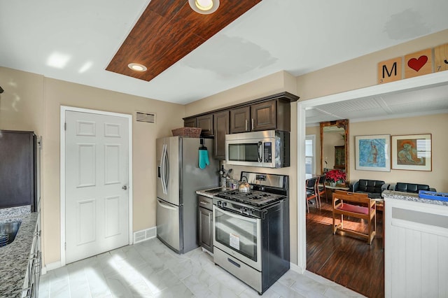 kitchen featuring dark brown cabinets, light stone countertops, and appliances with stainless steel finishes