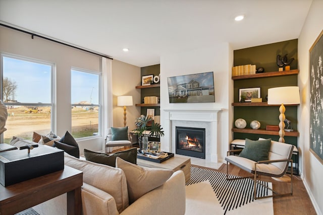 living room with a fireplace with flush hearth, wood finished floors, recessed lighting, and built in shelves