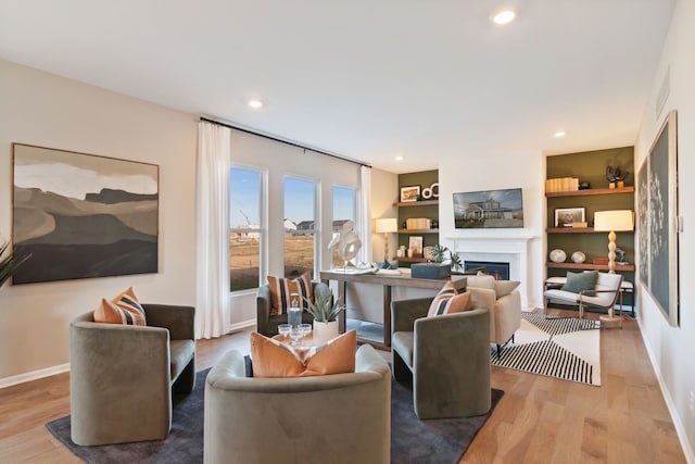 living area featuring built in shelves, baseboards, recessed lighting, a fireplace, and wood finished floors