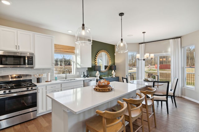 kitchen featuring light countertops, decorative backsplash, appliances with stainless steel finishes, wood finished floors, and a sink