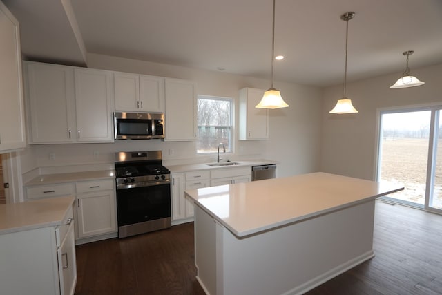 kitchen with dark wood-style floors, a sink, stainless steel appliances, light countertops, and a center island