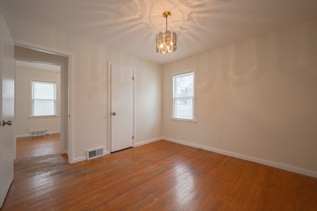 empty room with a notable chandelier and hardwood / wood-style flooring