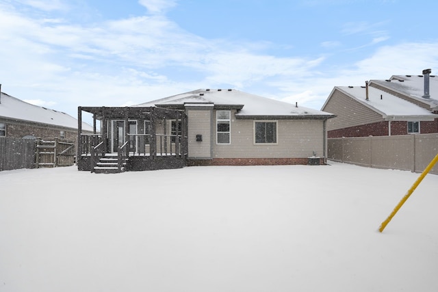 snow covered rear of property with a wooden deck and a pergola