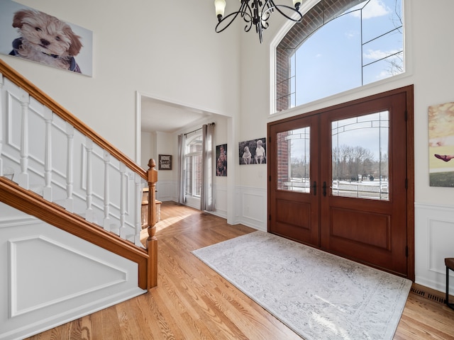 foyer entrance with a notable chandelier, a towering ceiling, light hardwood / wood-style flooring, and a wealth of natural light