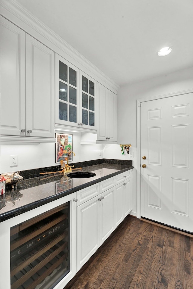 bar featuring sink, dark stone countertops, white cabinets, dark hardwood / wood-style flooring, and beverage cooler