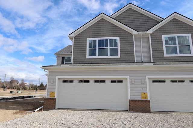 exterior space with a garage, brick siding, gravel driveway, and roof with shingles