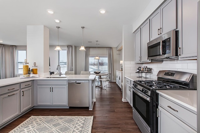 kitchen featuring appliances with stainless steel finishes, a sink, light countertops, gray cabinets, and dark wood-type flooring