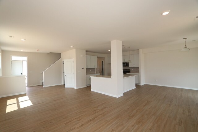 unfurnished living room featuring recessed lighting, baseboards, stairway, and light wood-type flooring