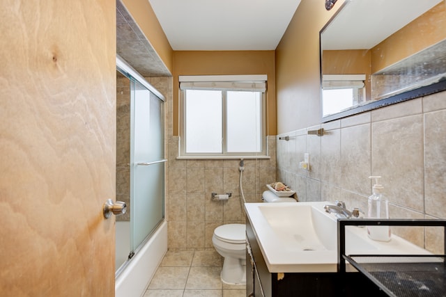 full bathroom with combined bath / shower with glass door, tile walls, tile patterned flooring, vanity, and toilet