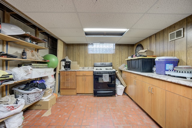 kitchen with a drop ceiling, range with gas stovetop, and wooden walls