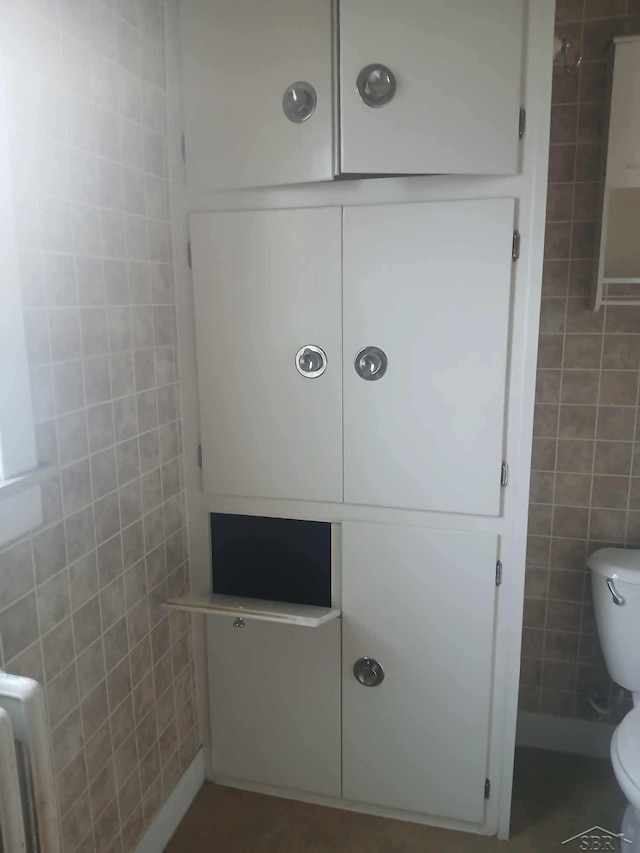 bathroom with radiator heating unit, tile walls, and toilet