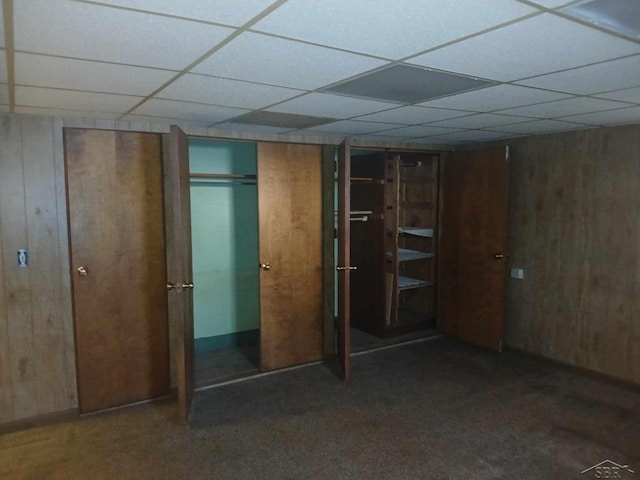 interior space with dark colored carpet, a paneled ceiling, and wood walls