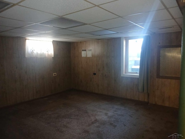 basement featuring a paneled ceiling, wooden walls, and dark carpet