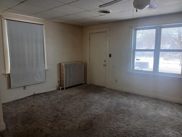 carpeted spare room with radiator, a drop ceiling, and ceiling fan