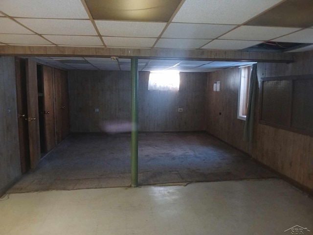 basement with a drop ceiling and wood walls