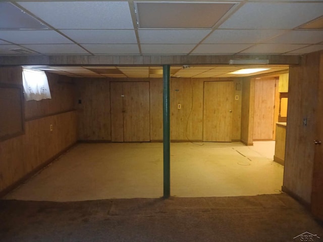 basement with a drop ceiling and wood walls