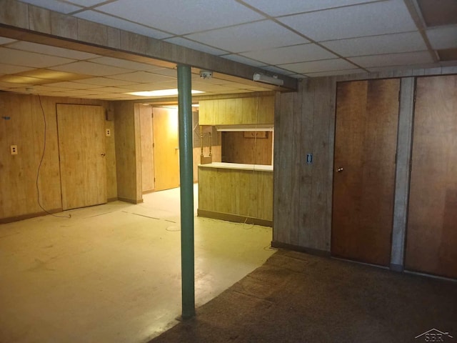 basement featuring a paneled ceiling and wooden walls