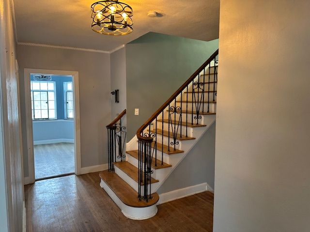 stairs with an inviting chandelier, hardwood / wood-style floors, and ornamental molding