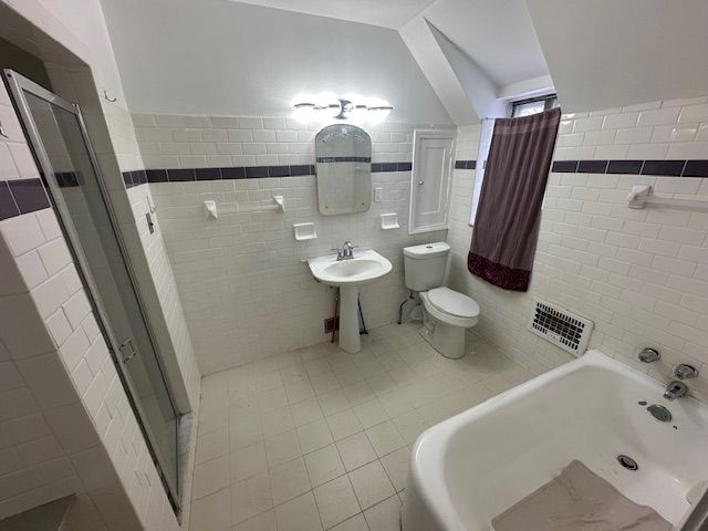 bathroom with tile patterned flooring, a shower with shower door, tile walls, and toilet