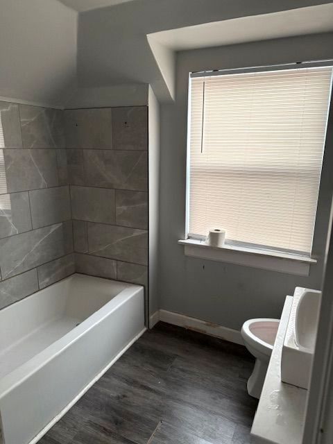 bathroom featuring a healthy amount of sunlight, hardwood / wood-style floors, tiled shower / bath combo, and toilet