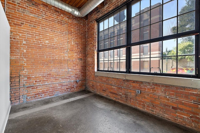 spare room with concrete floors, a high ceiling, and brick wall