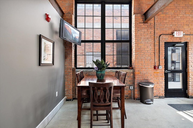 dining space featuring beamed ceiling, brick wall, and concrete flooring