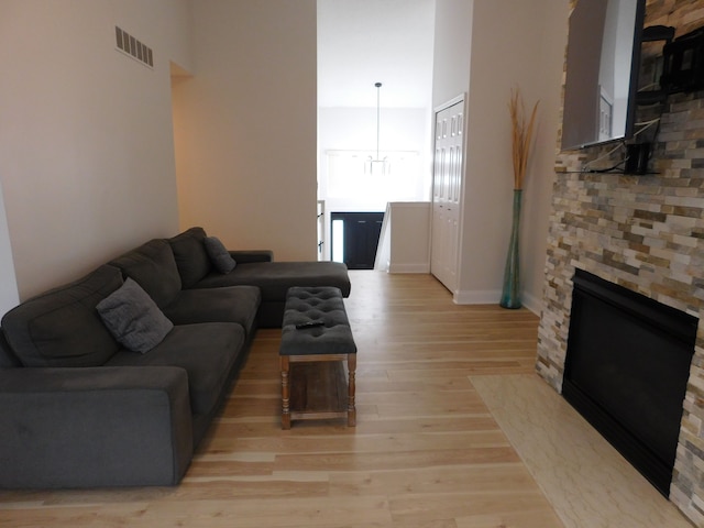 living room with a stone fireplace, a chandelier, and light wood-type flooring