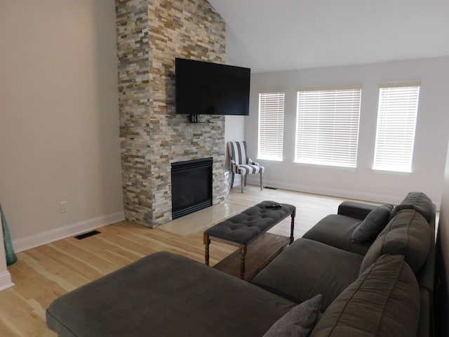 living room featuring lofted ceiling, a stone fireplace, and light wood-type flooring