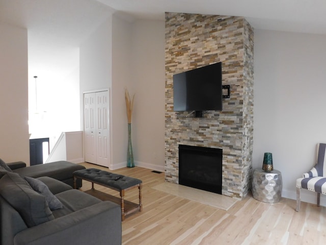 living room featuring a stone fireplace, vaulted ceiling, and light wood-type flooring