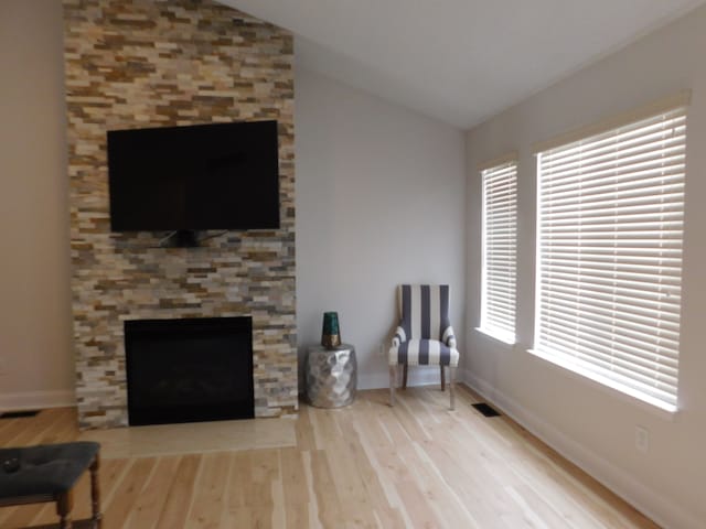 living room with a stone fireplace, vaulted ceiling, and light wood-type flooring